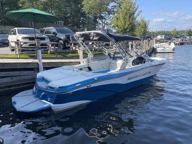 MasterCraft XT23 2021 MasterCraft XT23 boat docked on a sunny day, featuring sleek blue and white design.