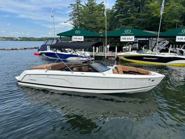 Cobalt CS23 2024 Cobalt CS23 boat for sale, docked on a serene lake with green canopies.