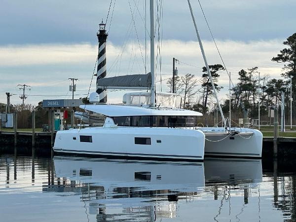 Lagoon 42 2017 Lagoon 42 catamaran docked near a lighthouse, reflecting on calm water.
