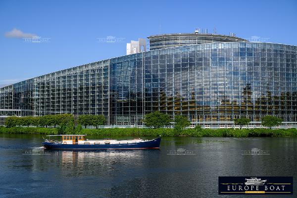 Luxe-Motor SRF 27.85 FRANCE PROOF BESPOKE A Luxe-Motor SRF 27.85 boat on a river, modern glass building backdrop.
