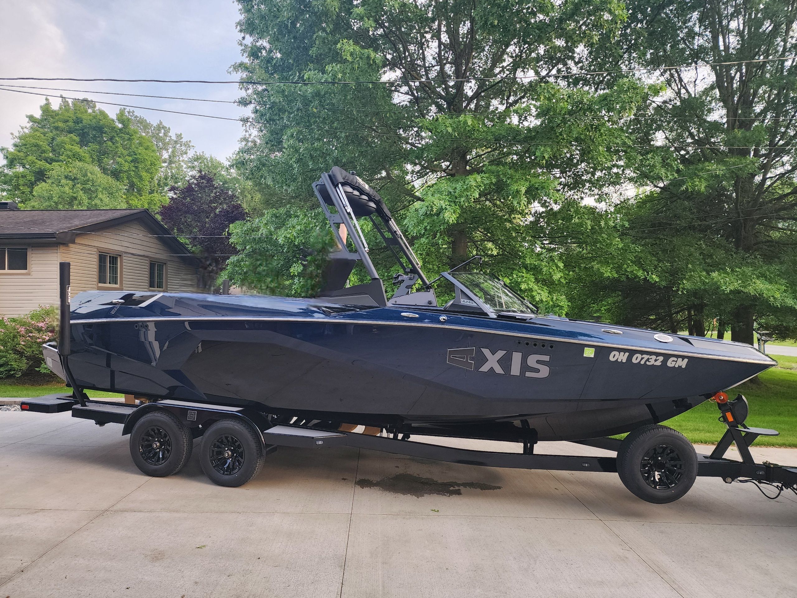 Axis A245 2024 Axis A245 boat on trailer, parked in driveway with lush green trees in background.