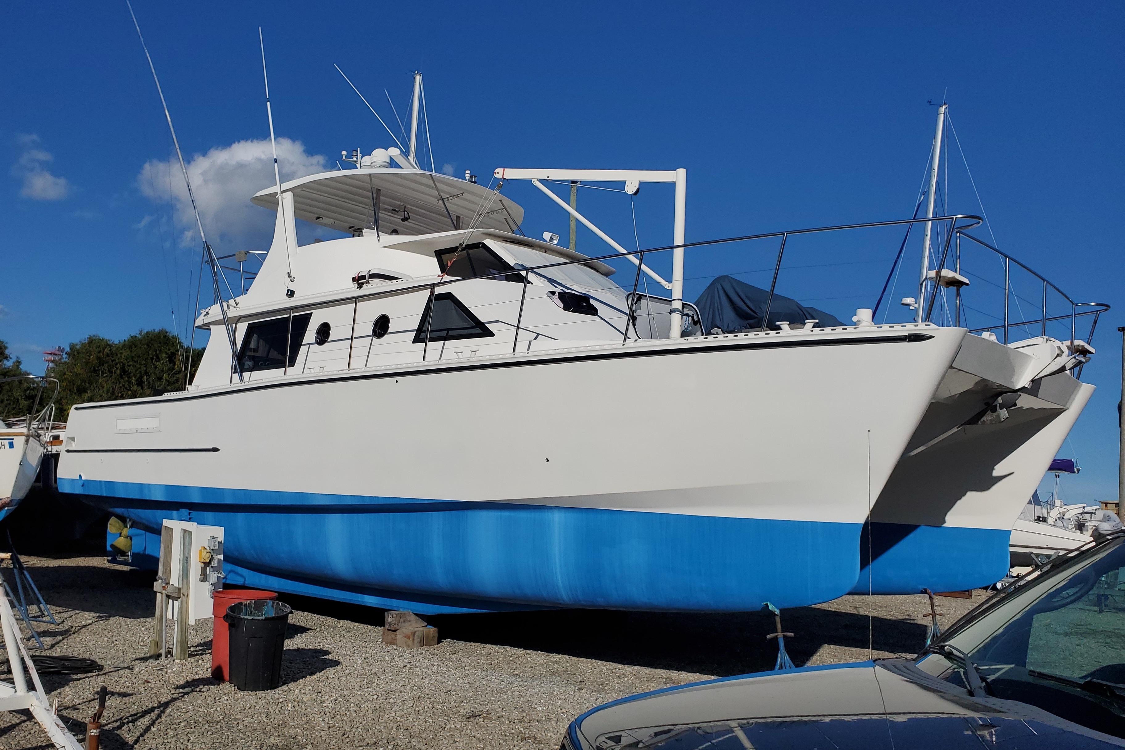 Custom Sea Raider Catamaran Custom 2005 Sea Raider Catamaran with blue hull, docked on gravel under clear sky.
