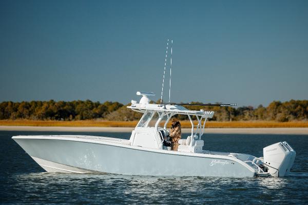 Yellowfin 32 2025 Yellowfin 32 boat cruising on calm water near a wooded shoreline.