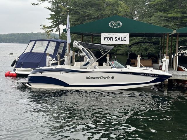 MasterCraft X24 2023 MasterCraft X24 boat docked, for sale sign visible, surrounded by trees and water.