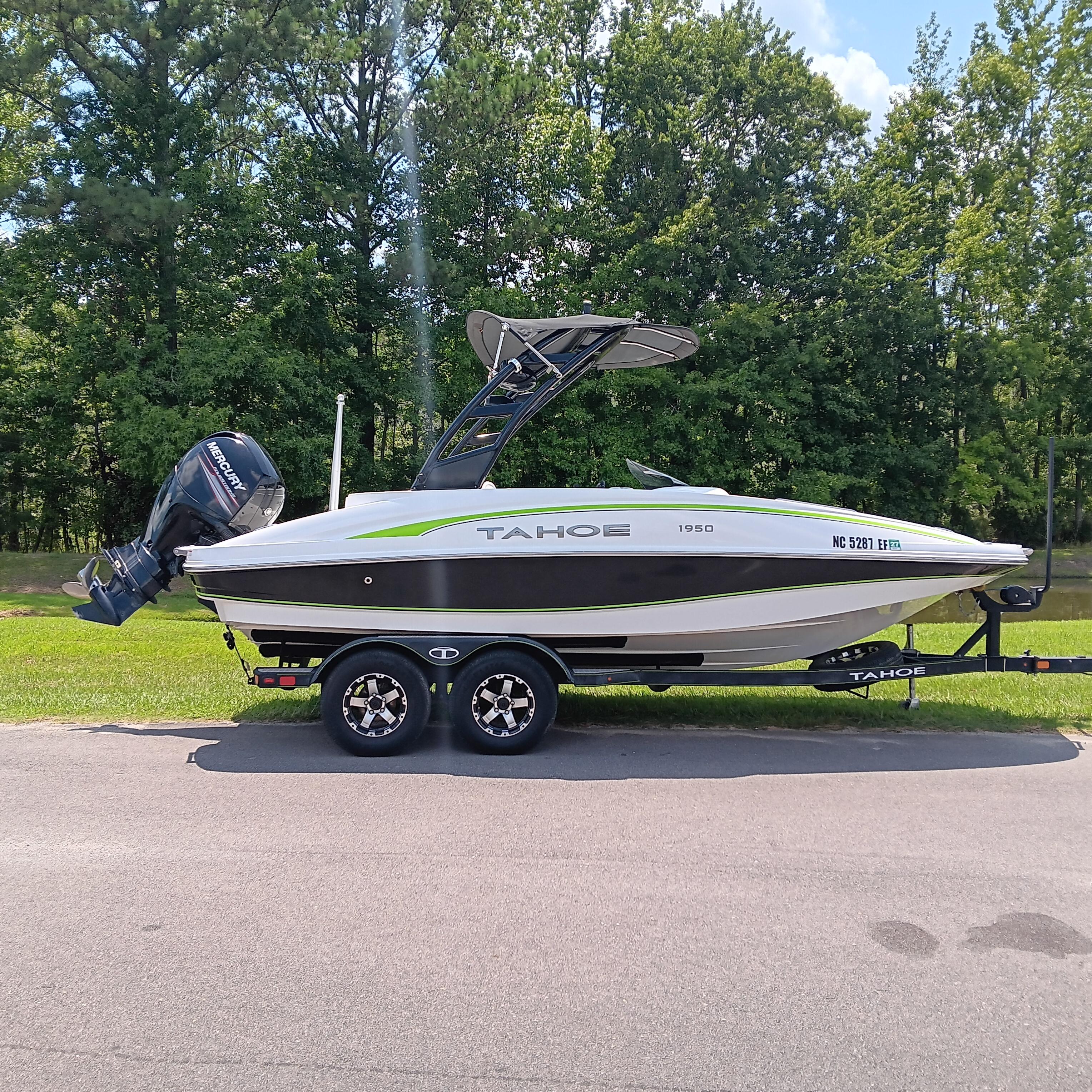 Tahoe 1950 2017 Tahoe 1950 boat on trailer, parked on road with green trees in background.