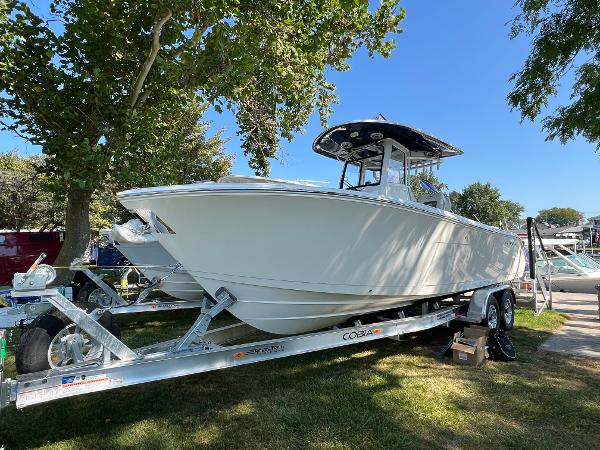 Cobia 265 CC 2025 Cobia 265 CC boat on trailer under trees, sunny day.