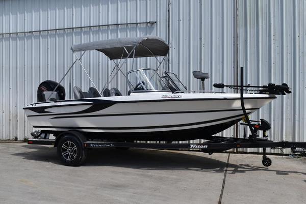 Triton 186 Allure 2024 Triton 186 Allure boat with canopy on trailer, parked by metal building.