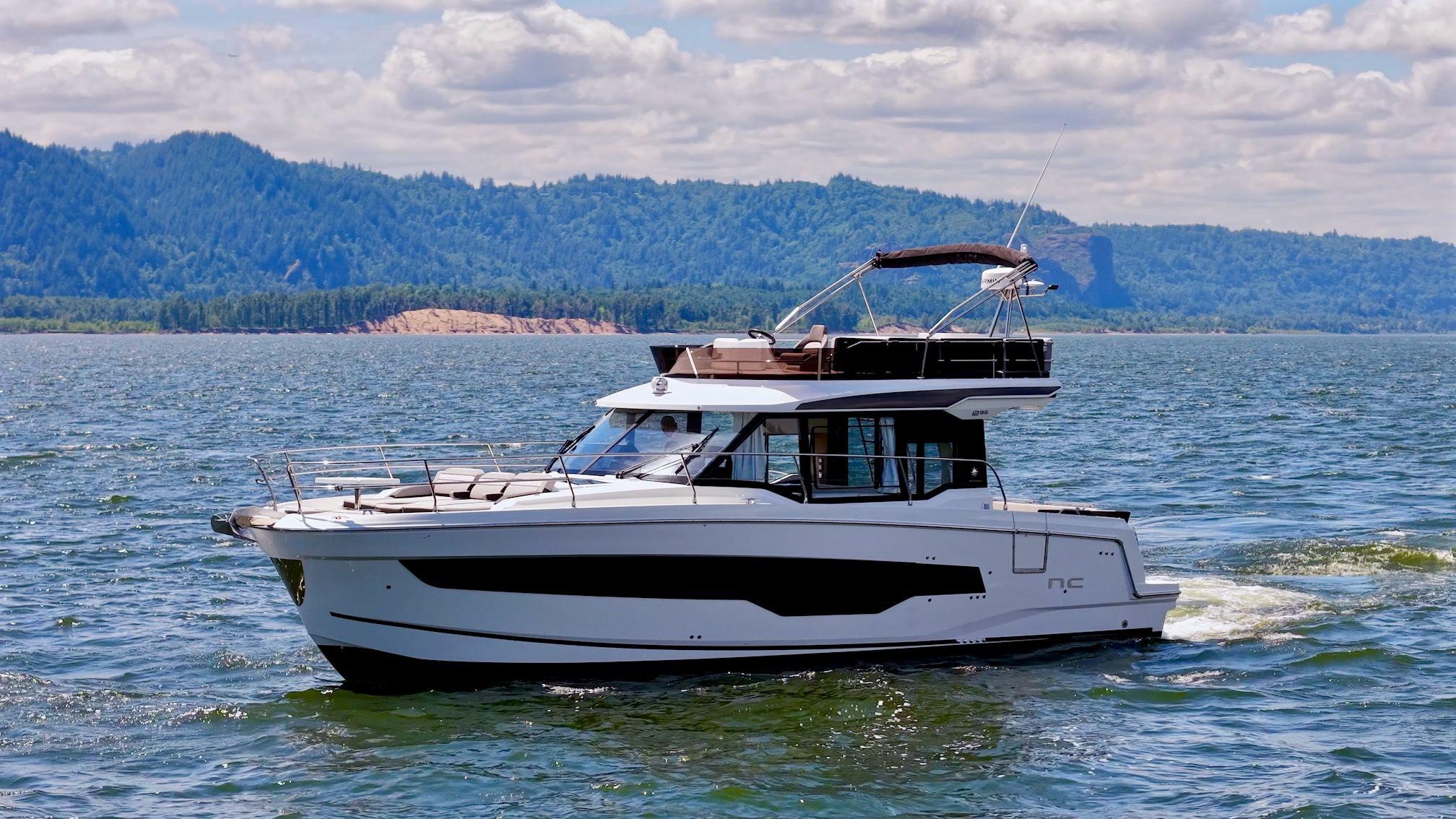 Jeanneau NC 1295 Fly 2025 Jeanneau NC 1295 Fly yacht cruising on a scenic lake with mountains.