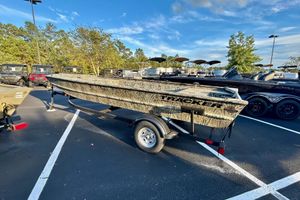 Tracker Grizzly 1860 Utility 2026 Tracker Grizzly 1860 Utility boat on trailer in parking lot, surrounded by trees.