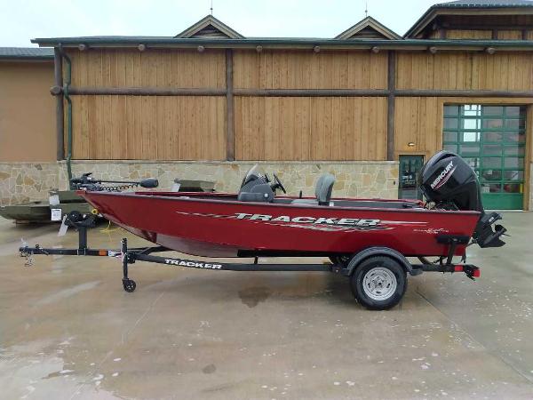 Tracker Super Guide V-16 SC 2025 Tracker Super Guide V-16 SC boat, red, on trailer, parked outside wooden building.
