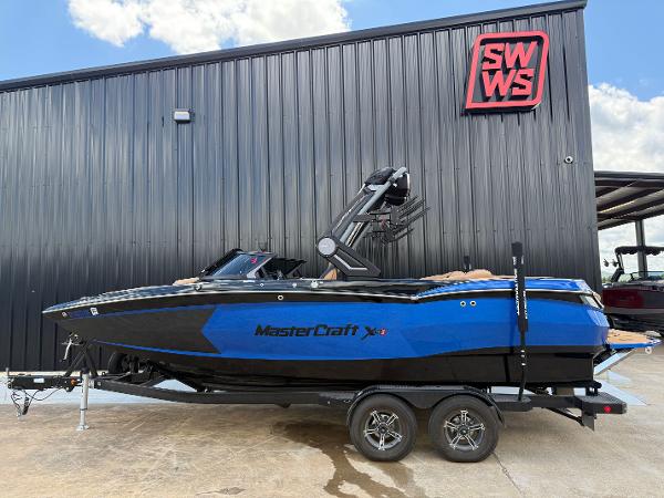 MasterCraft XStar S 2023 MasterCraft XStar S boat in blue, parked on a trailer outside a black building.