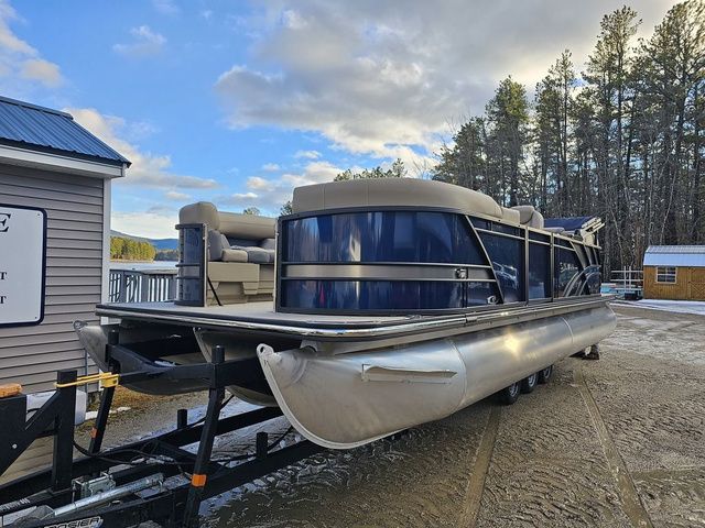 Sylvan X5 2024 Sylvan X5 pontoon boat on trailer, parked near a lake with trees in the background.