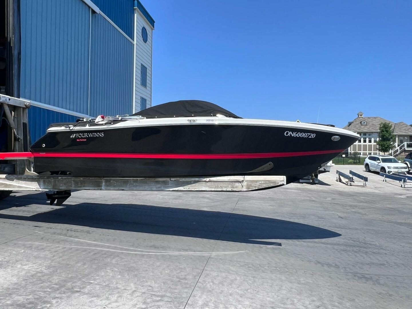 Four Winns H210 2016 Four Winns H210 boat on trailer, black with red stripe, near blue building.