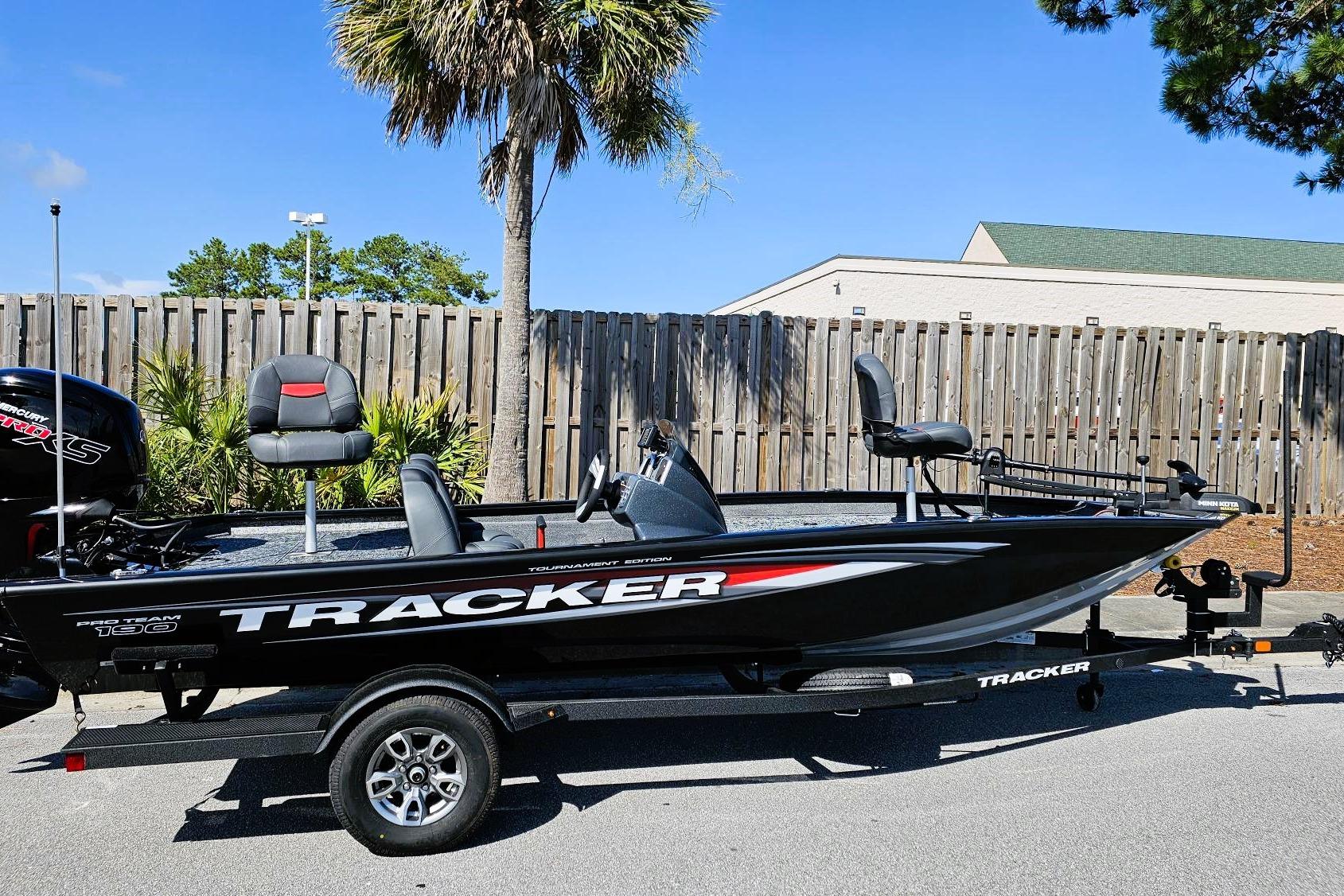 Tracker Pro Team 190 2026 Tracker Pro Team 190 boat on trailer, parked outdoors near wooden fence.