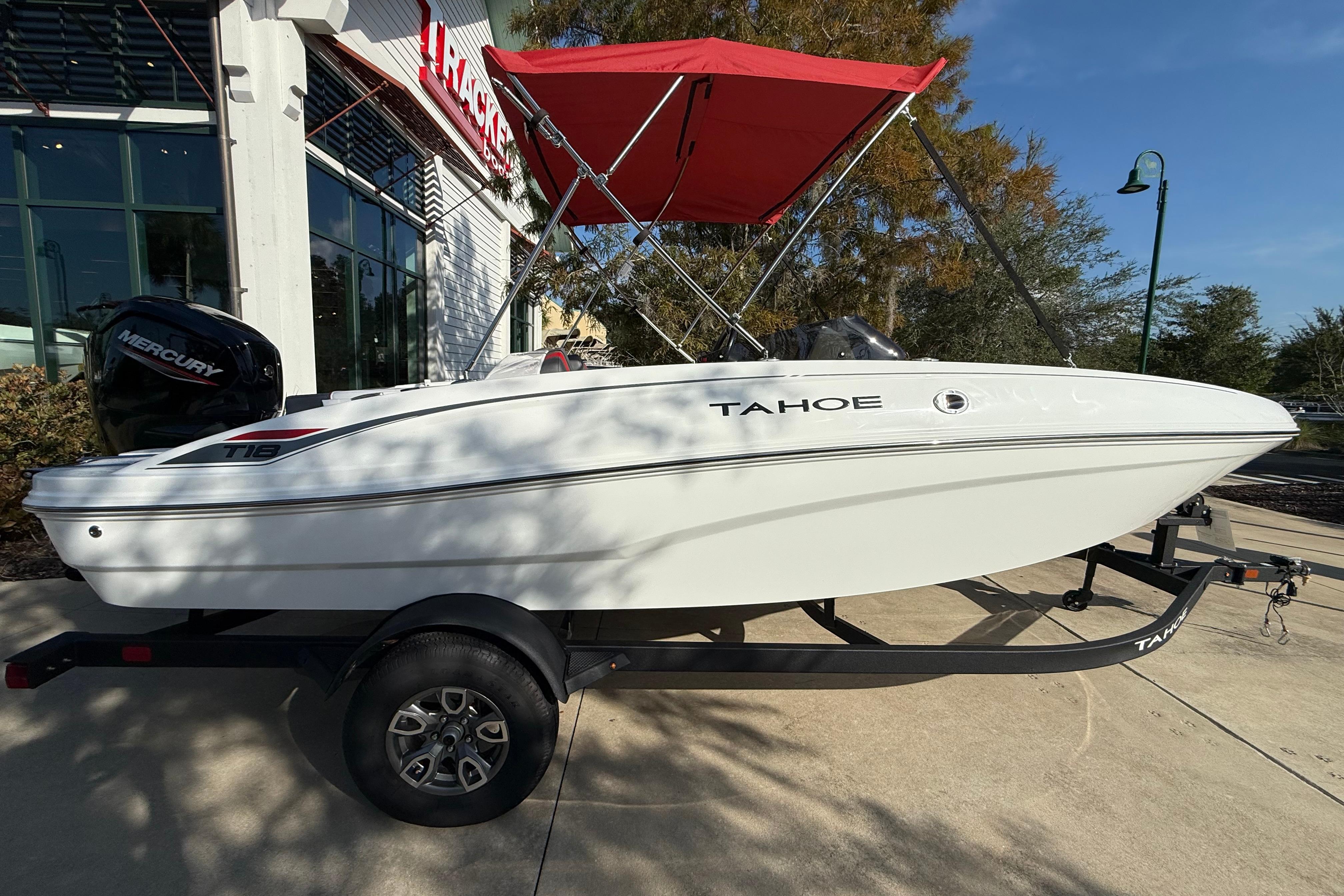 Tahoe T18 2025 Tahoe T18 boat with red canopy on trailer, parked outside a building.