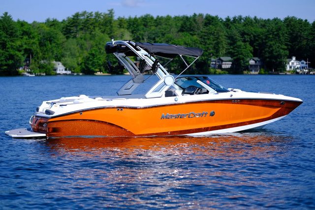 MasterCraft X22 2023 MasterCraft X22 boat on a lake with lush green trees in the background.