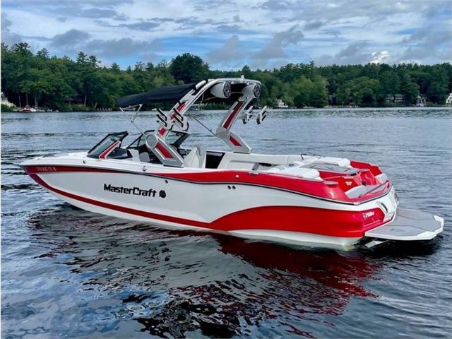 MasterCraft X24 2022 MasterCraft X24 boat on a lake with lush green forest background.