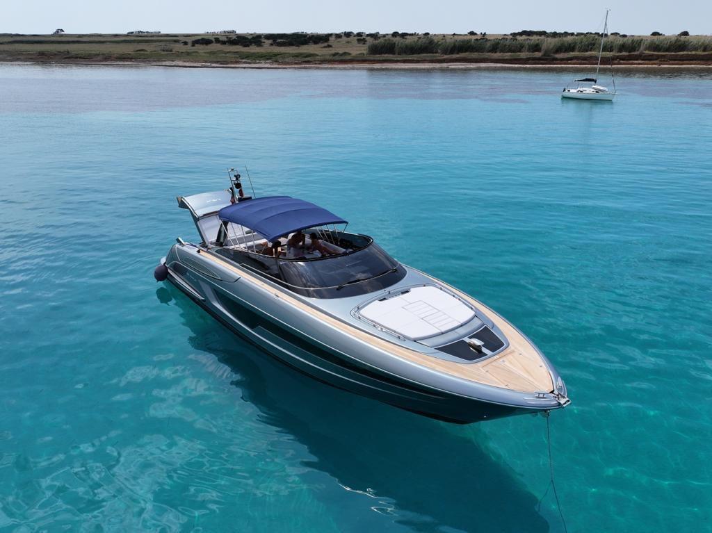 Riva 56 RIVALE 2023 Riva 56 Rivale yacht on clear turquoise water, featuring sleek design and blue canopy.