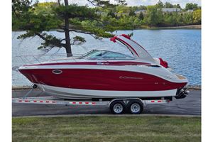Crownline 270 CR 2023 Crownline 270 CR boat on trailer by a lake, featuring sleek red and white design.
