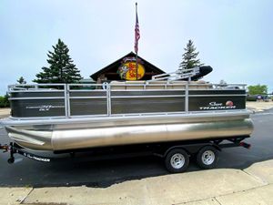 Sun Tracker Fishin' Barge 20 DLX 2025 Sun Tracker Fishin' Barge 20 DLX pontoon boat on trailer, parked outside.