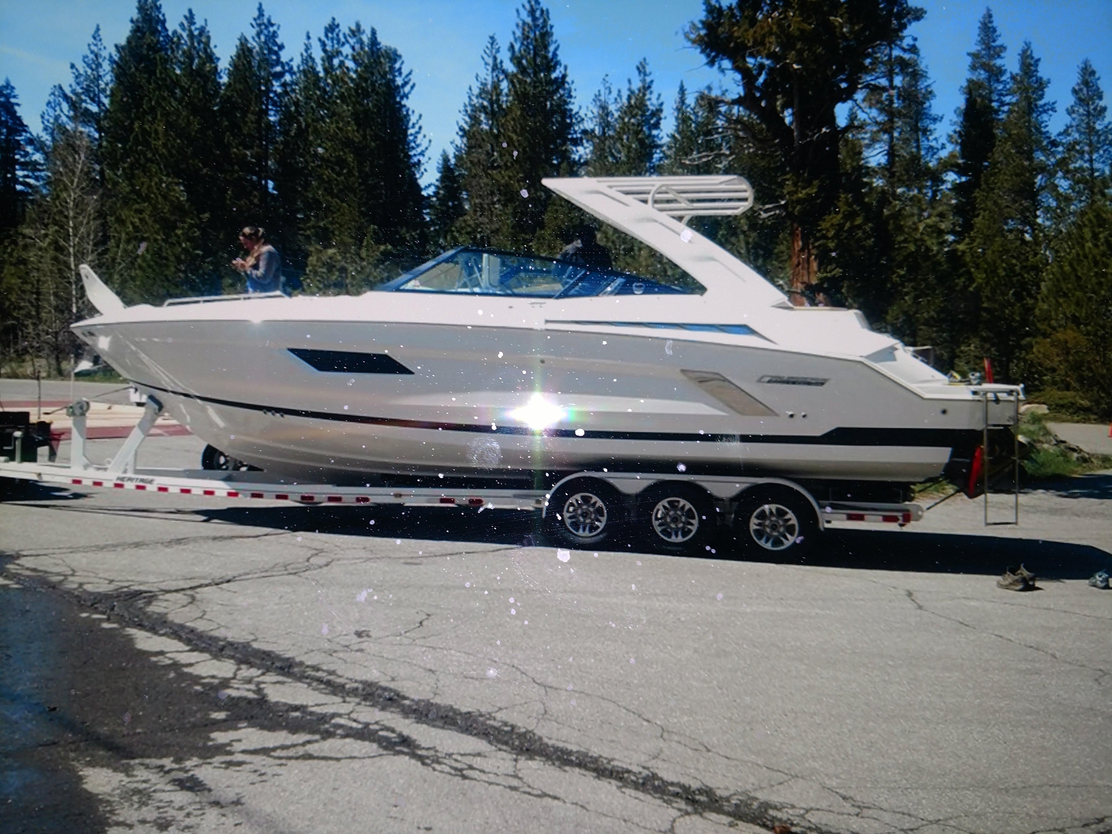 Cruisers Yachts 328CX 2015 Cruisers Yachts 328CX on trailer, surrounded by trees, in a parking area.