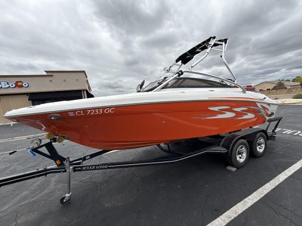 Four Winns H220 2008 Four Winns H220 boat on trailer, orange with white accents, parked outdoors.