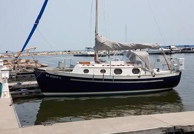 Pacific Seacraft Dana 24 1987 Pacific Seacraft Dana 24 sailboat docked at marina, blue hull, covered sails.