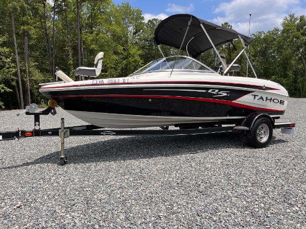 Tahoe Q5i 2014 Tahoe Q5i boat on trailer, parked on gravel, surrounded by trees.