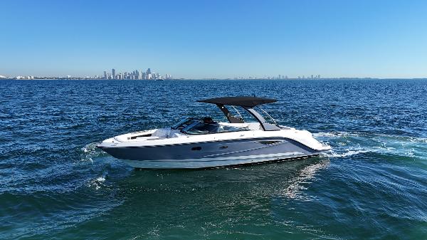 Sea Ray SLX 310 2019 Sea Ray SLX 310 boat cruising on open water with city skyline in background.