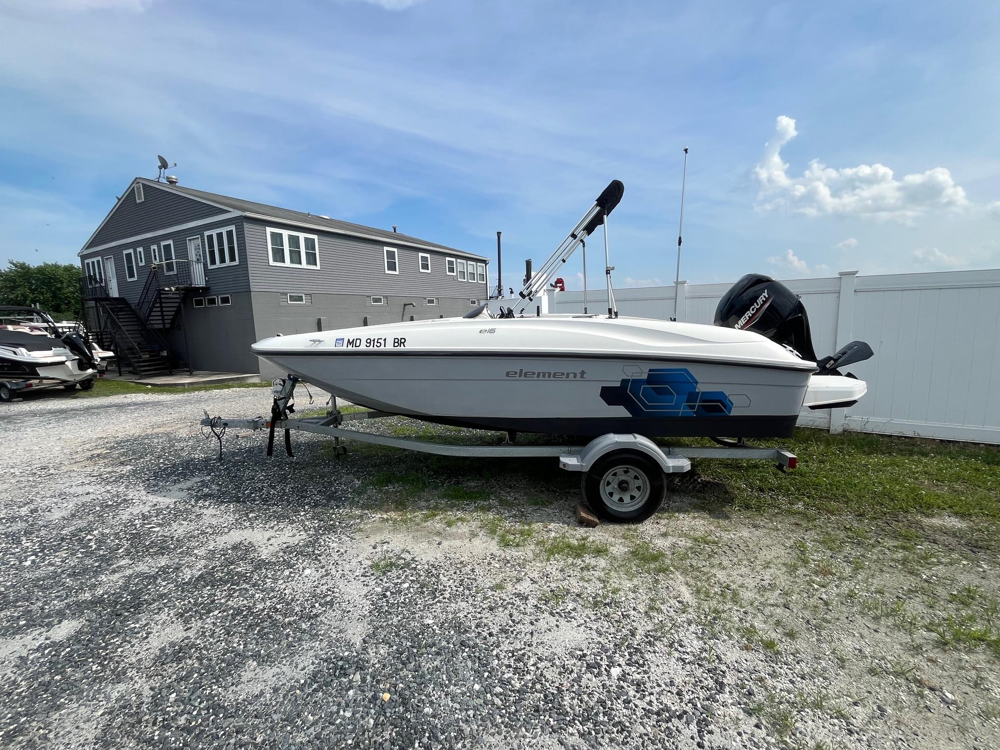 Bayliner Element E16 2021 Bayliner Element E16 boat on trailer, parked near a building under a clear sky.