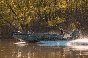 Excel 1751 Viper F4 Man driving Excel 2172 Stalker CC boat on a calm river, surrounded by autumn trees.