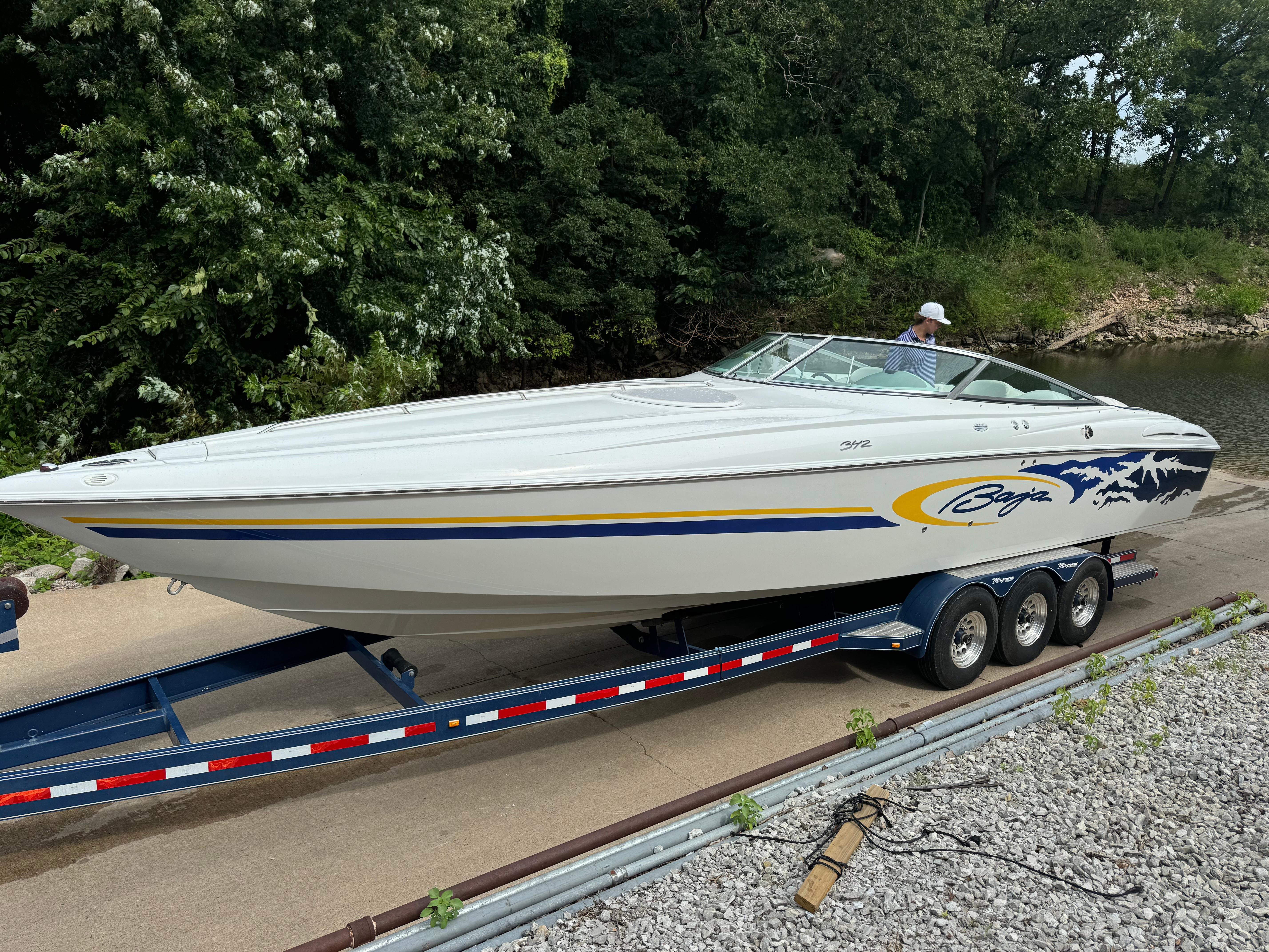 Baja 342 2002 Baja 342 speedboat on trailer, parked near lush greenery.