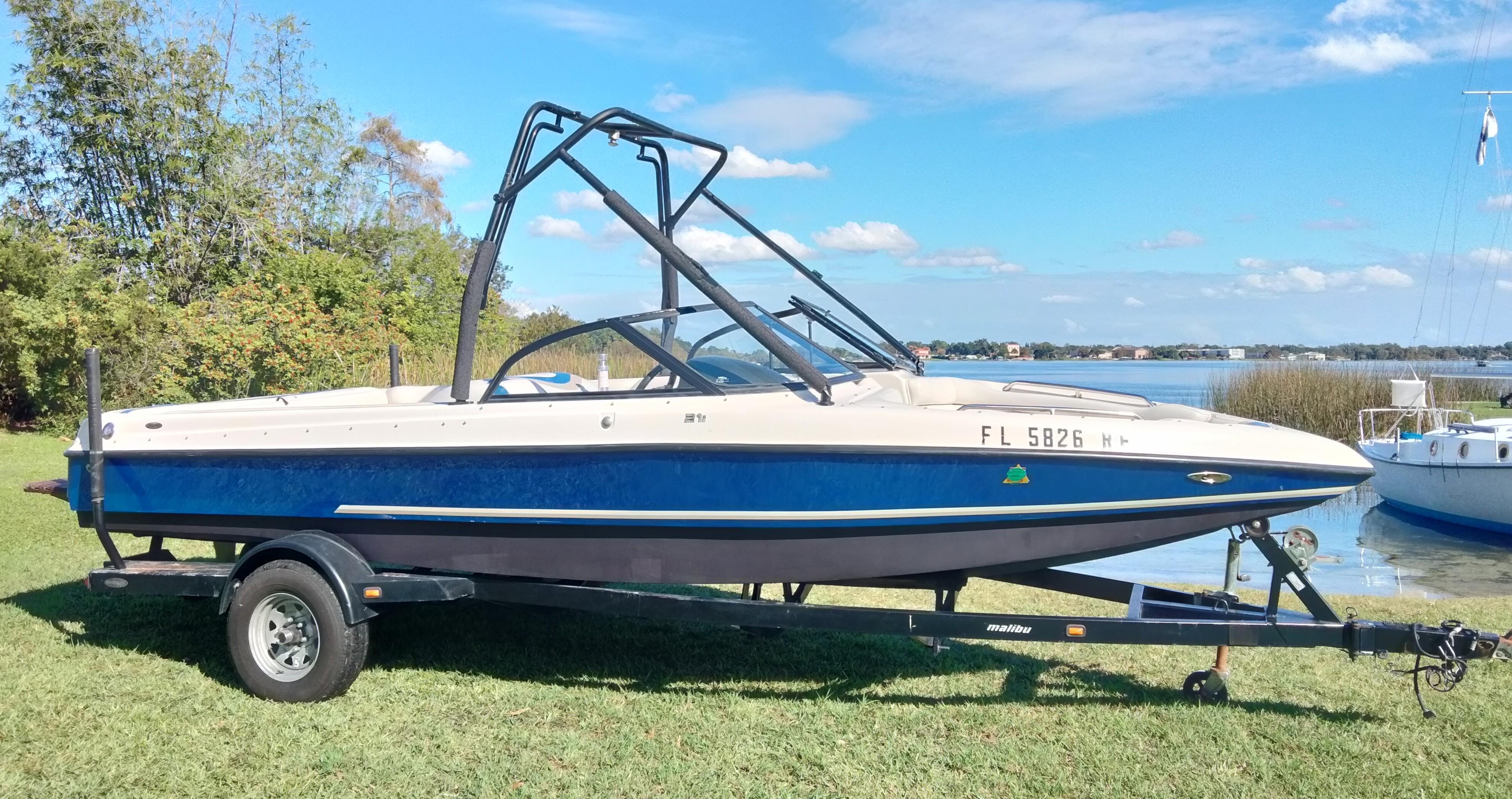 Tigé 21i 2001 Tigé 21i boat on trailer by a lake, under a clear blue sky.