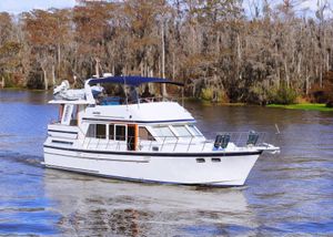 Jefferson Sundeck 1987 Jefferson Sundeck yacht cruising on a scenic river with lush forest backdrop.