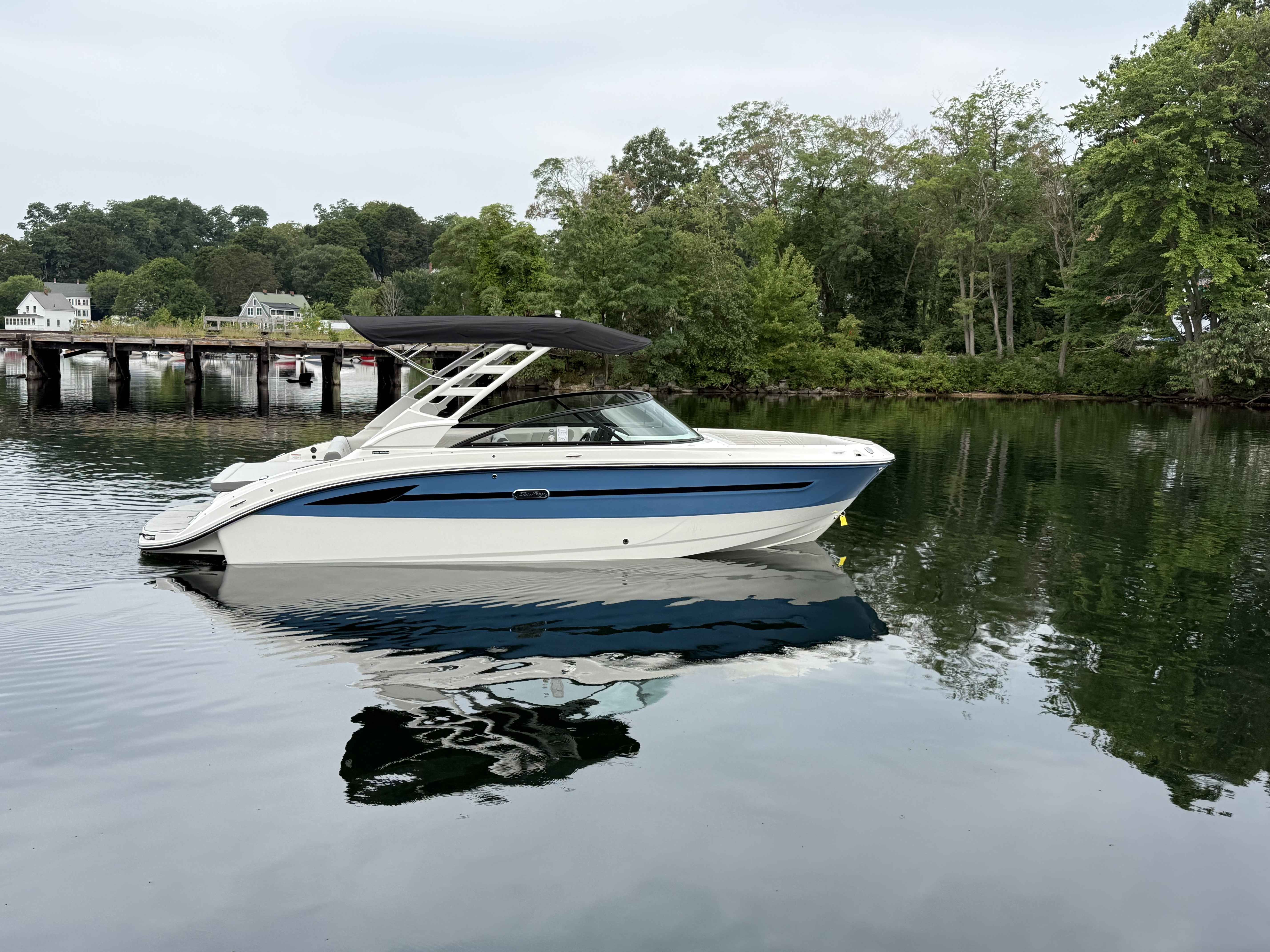 Sea Ray 250SDS 2026 Sea Ray 250SDS boat on calm water, surrounded by lush greenery and a bridge.