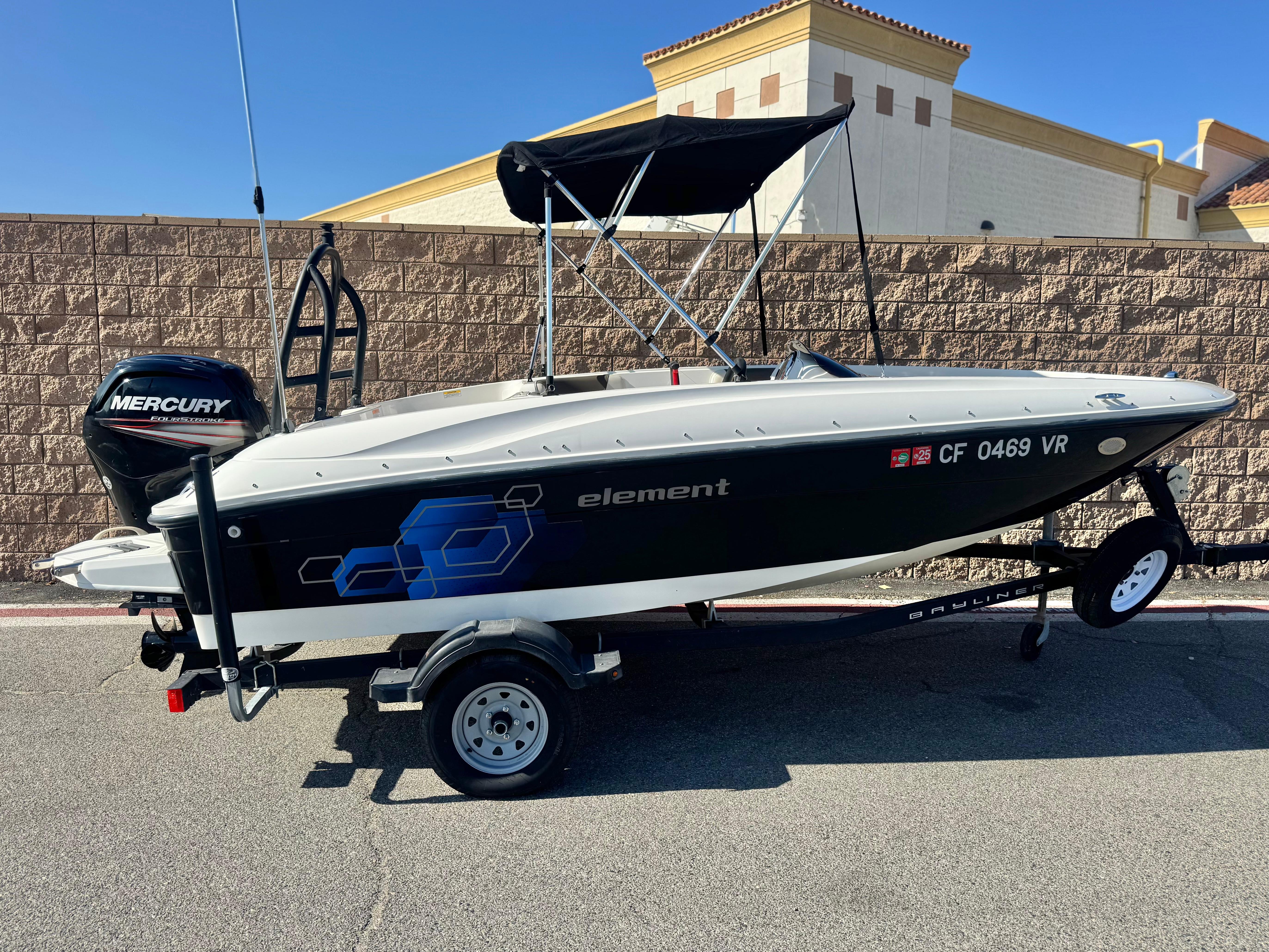 Bayliner Element E16 2019 Bayliner Element E16 boat with Mercury engine on trailer, parked by a brick wall.
