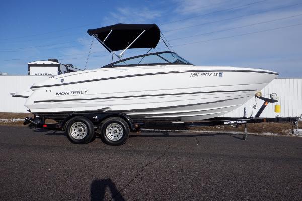 Monterey 224FS 2020 Monterey 224FS boat on trailer, white exterior, black canopy, parked on asphalt.