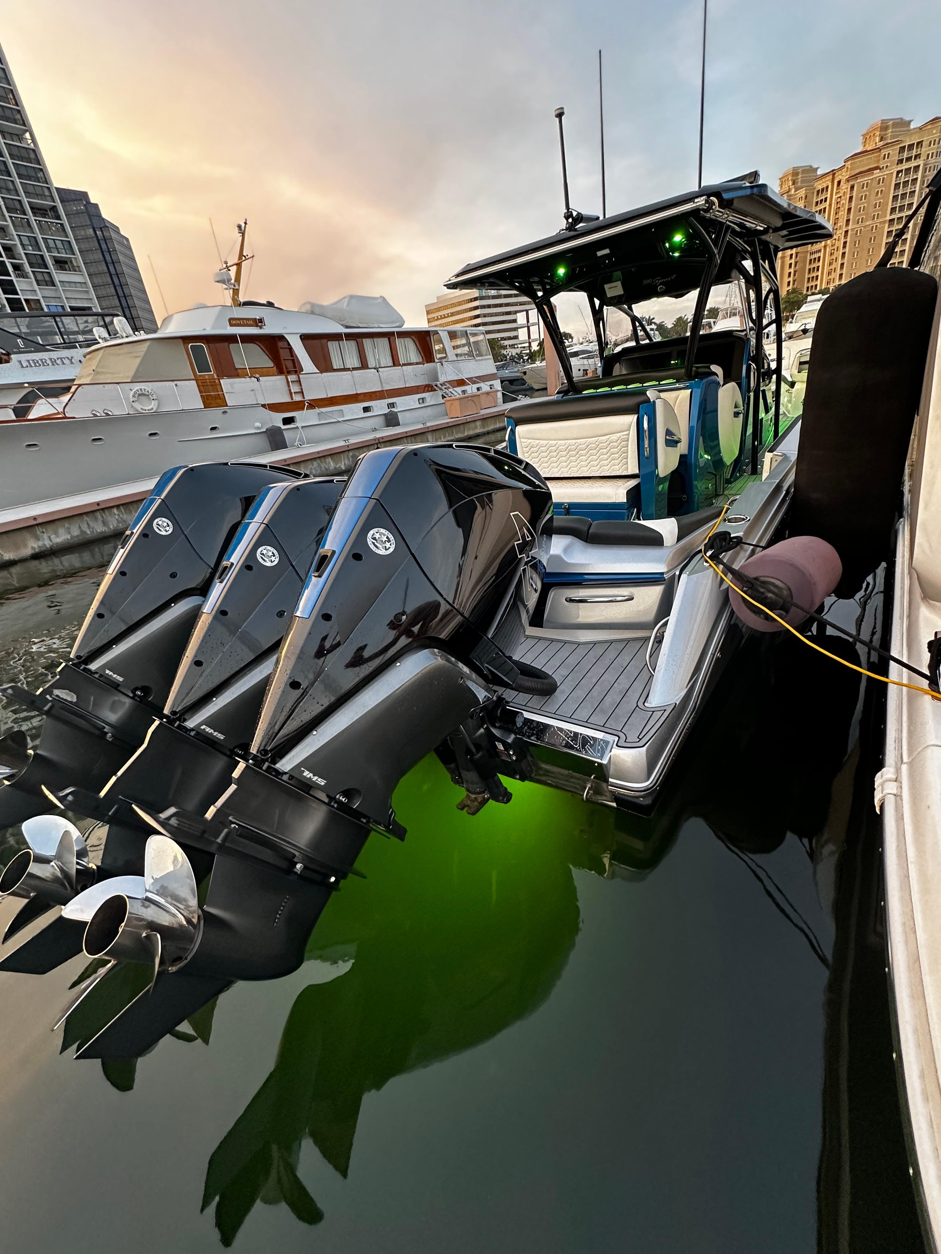 Nor-Tech 390 2022 Nor-Tech 390 boat docked, featuring triple outboard engines and illuminated green underwater lights.
