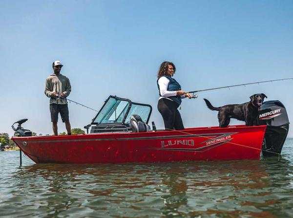 Lund 1650 Angler 2026 Lund 1650 Angler boat with two people and a dog fishing on a lake.