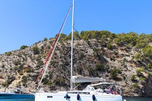 Beneteau Oceanis 38.1 2023 Beneteau Oceanis 38.1 sailboat anchored near rocky coastline under clear blue sky.