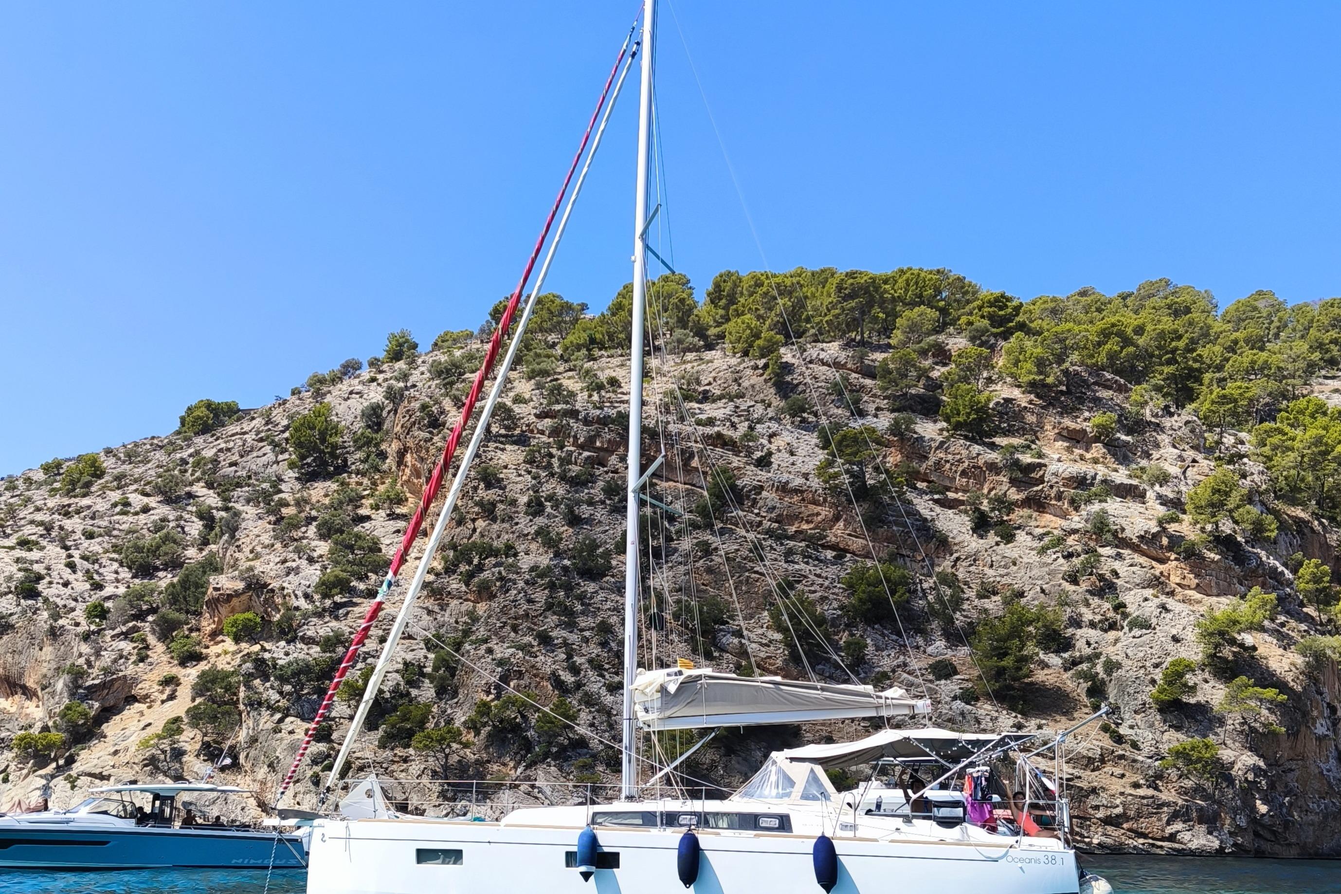 Beneteau Oceanis 38.1 2023 Beneteau Oceanis 38.1 sailboat anchored near rocky coastline under clear blue sky.