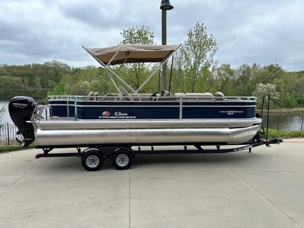 Sun Tracker Fishin' Barge 22 DLX 2025 Sun Tracker Fishin' Barge 22 DLX pontoon boat on trailer by a lake.