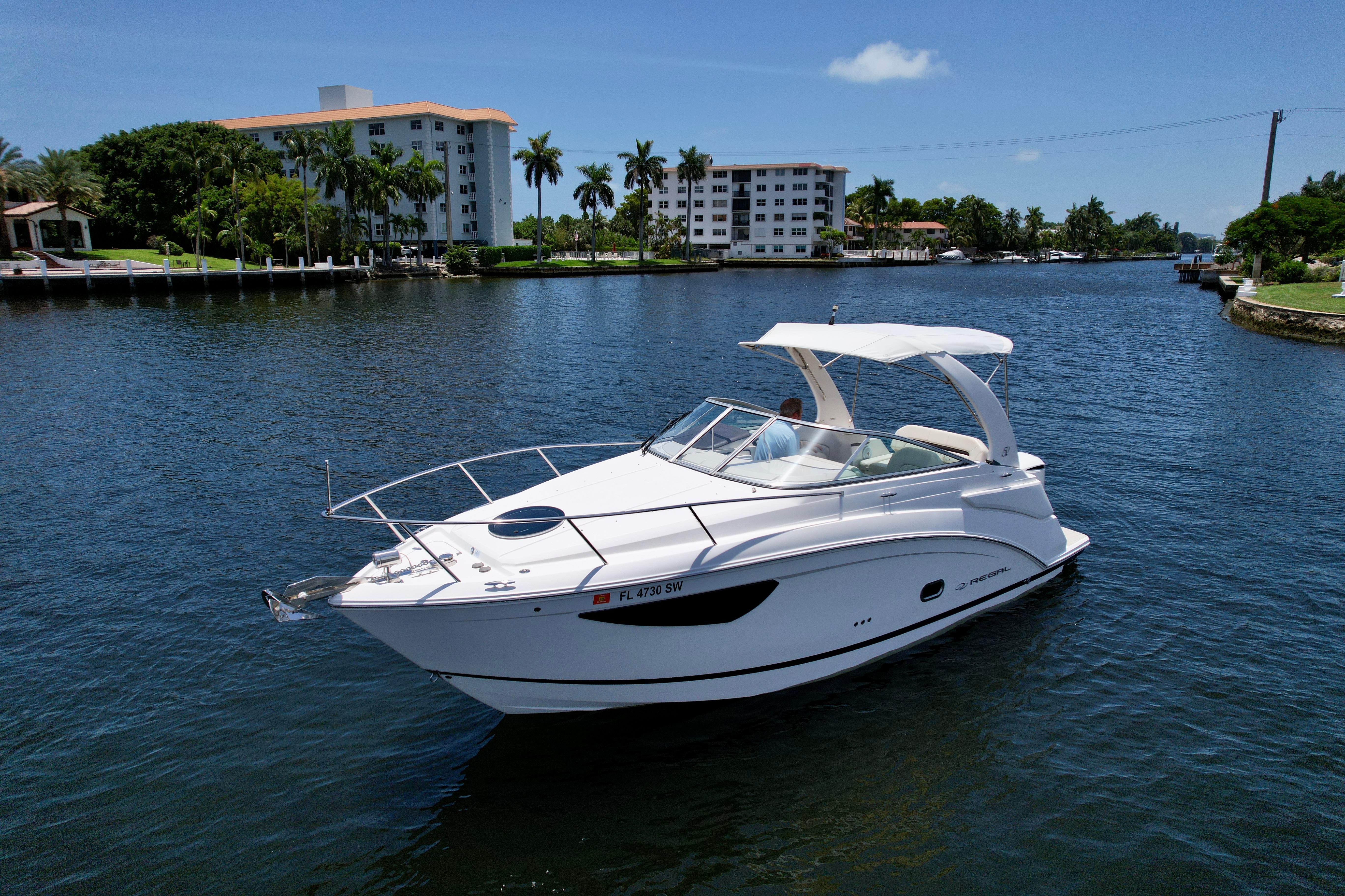 Regal 26 XO 2021 Regal 26 XO boat cruising on a sunny day near waterfront buildings and palm trees.