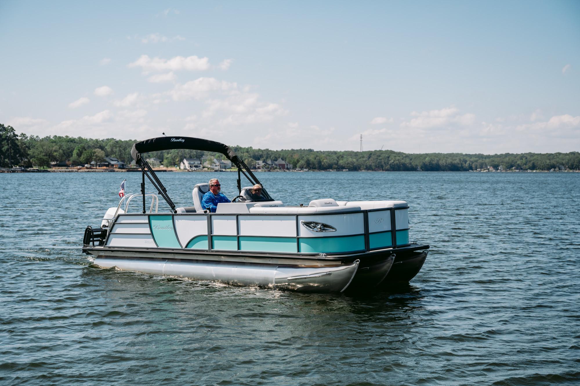 Bentley Pontoons Legacy QSB 2024 Bentley Pontoons Legacy QSB cruising on a serene lake under a clear blue sky.