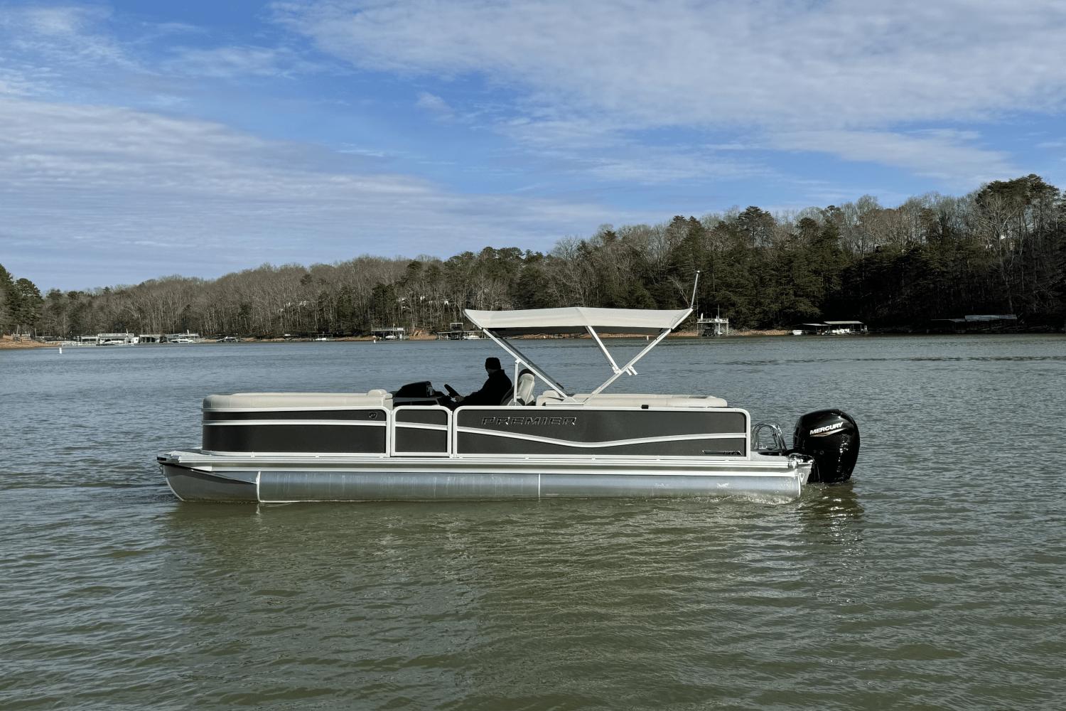 Premier 250 Sunsation 2024 Premier 250 Sunsation pontoon boat on a calm lake with a forested shoreline.