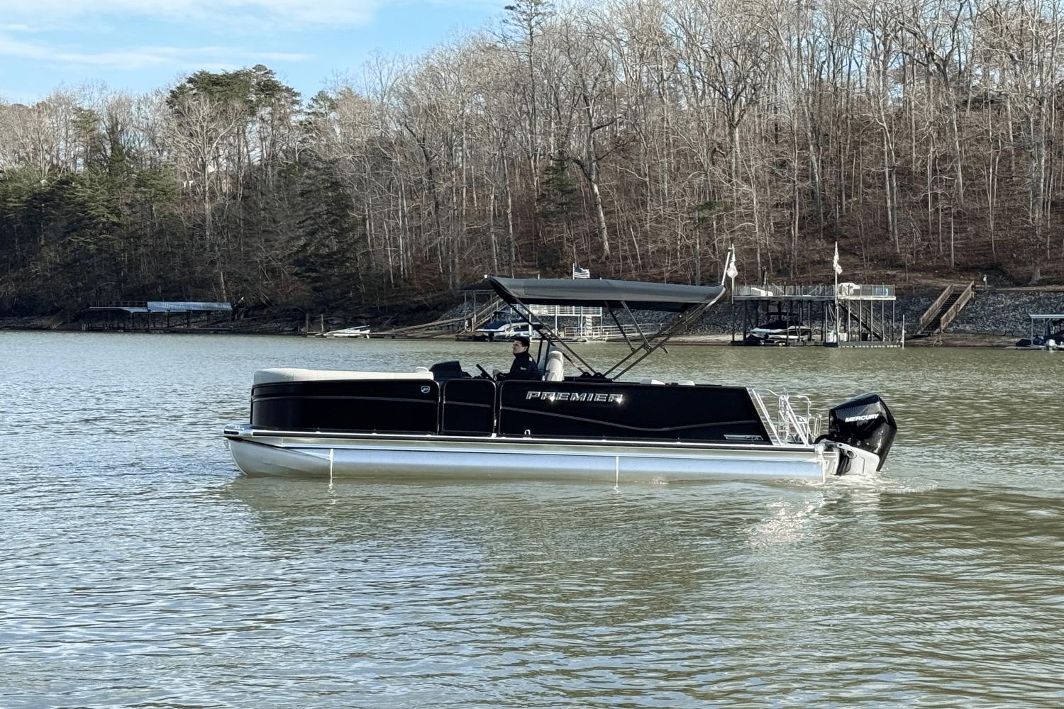 Premier 230 Solaris 2024 Premier 230 Solaris pontoon boat on a lake with wooded shoreline.