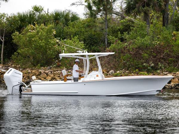 Custom Carolina 26 2024 Xcelerator Boatworks 26 on calm water, surrounded by lush greenery.