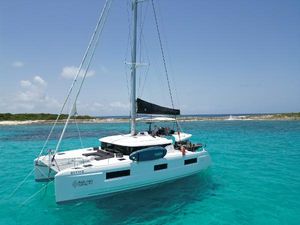 Lagoon 46 2023 Lagoon 46 catamaran sailing in clear turquoise waters near a sandy shoreline.