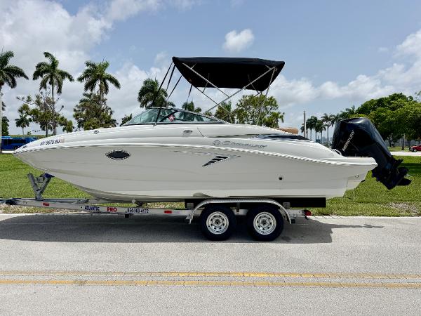 Crownline Eclipse E235 XS 2023 Crownline Eclipse E235 XS boat on trailer, parked roadside with palm trees in background.