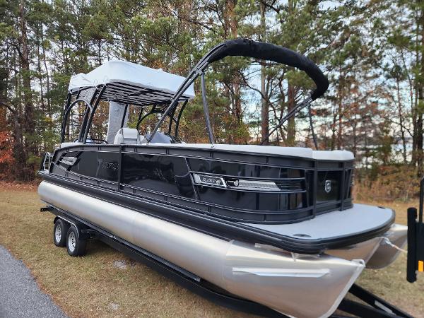 Godfrey AquaPatio Sundeck 275 SDC 2025 Godfrey AquaPatio Sundeck 275 SDC pontoon boat on trailer, parked near trees.